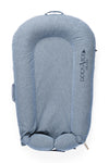 A blue DockATot LAST CHANCE: Deluxe+ Dock - Indigo Chambray baby lounger isolated on a white background. The lounger has a cushioned, oval shape with side handles and prominently displays the "DockATot" logo.